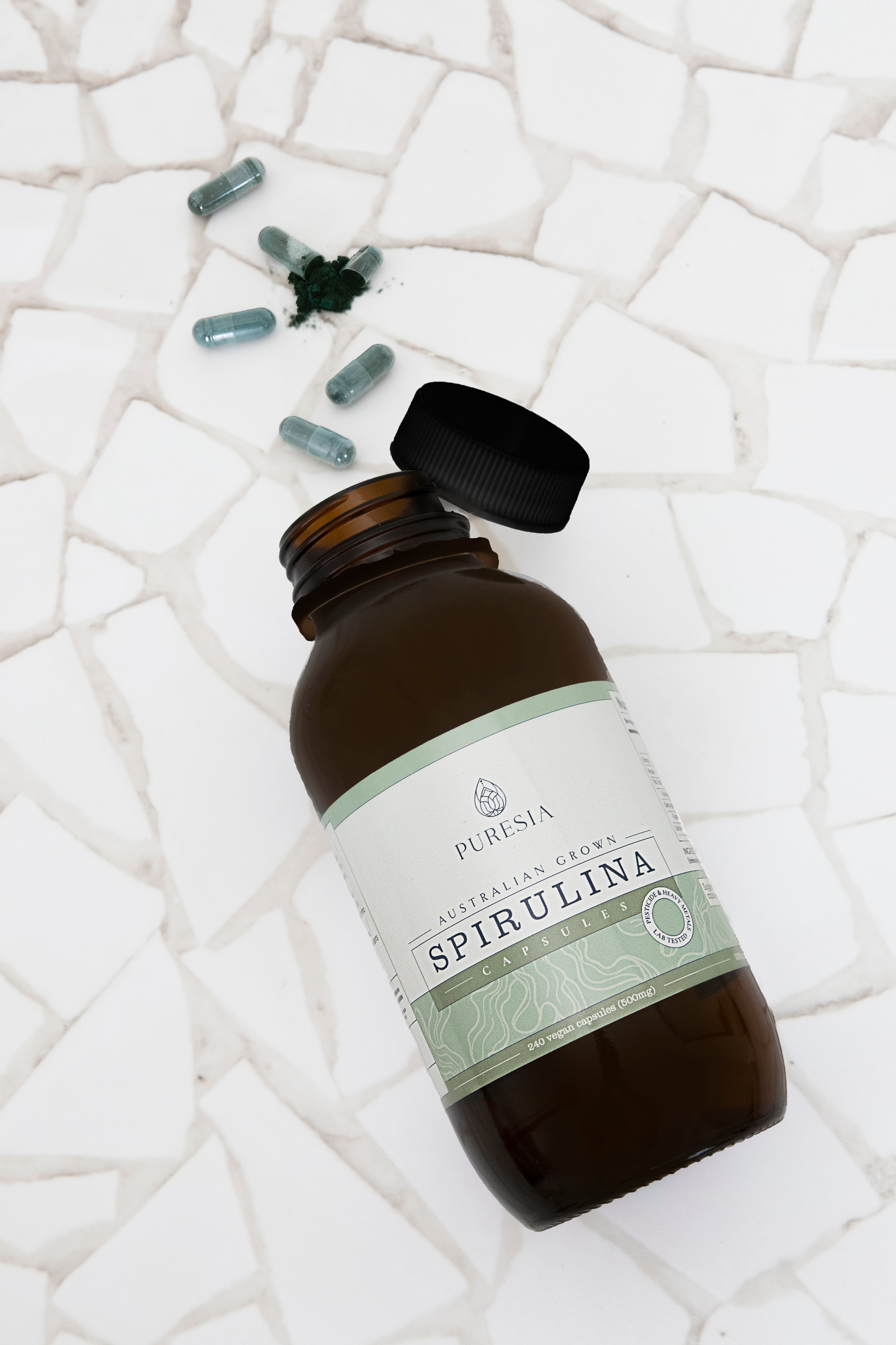 Bottle of Puresia Spirulina Capsules on a textured white surface