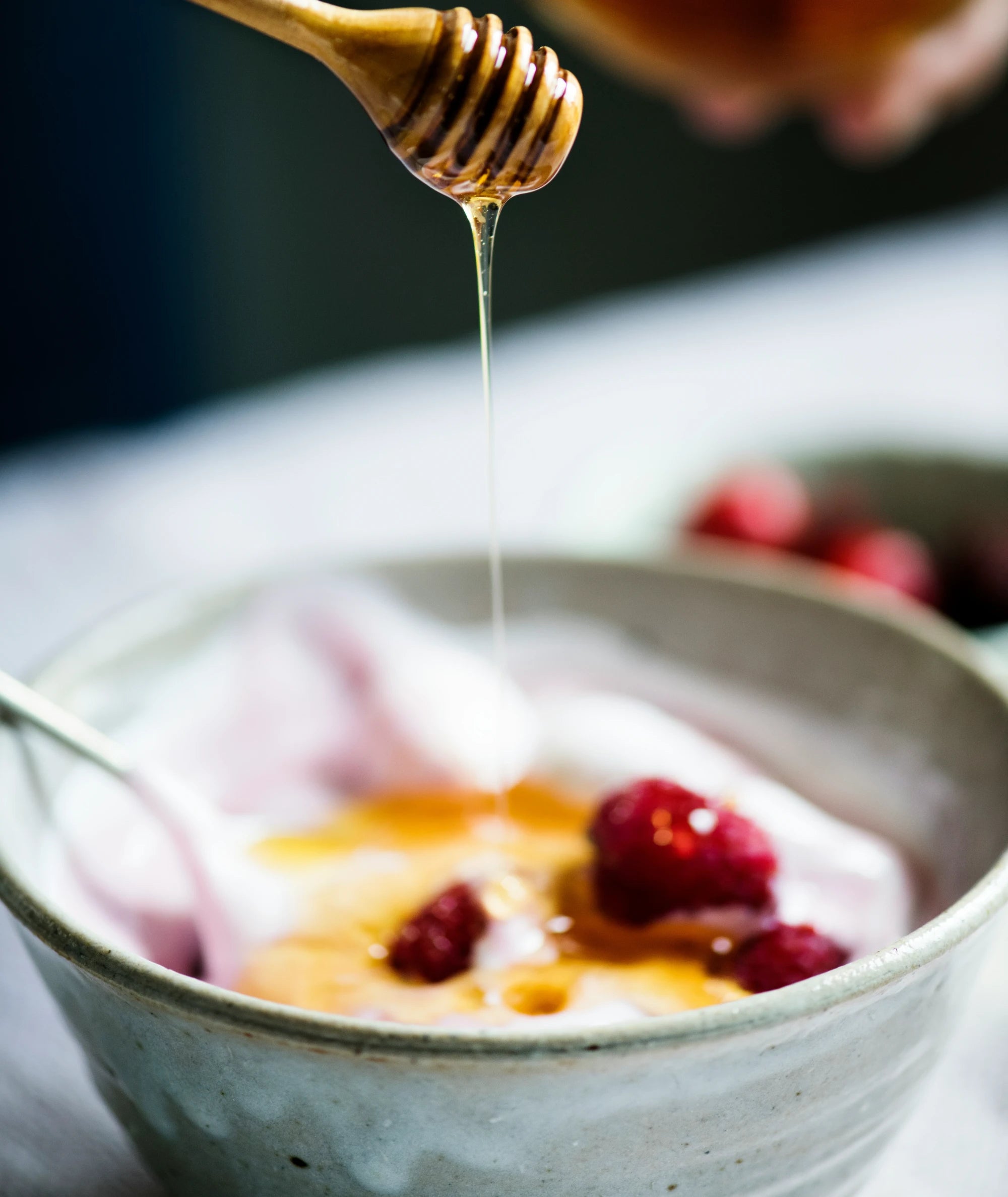 Honey being drizzled over a bowl of yogurt with raspberries